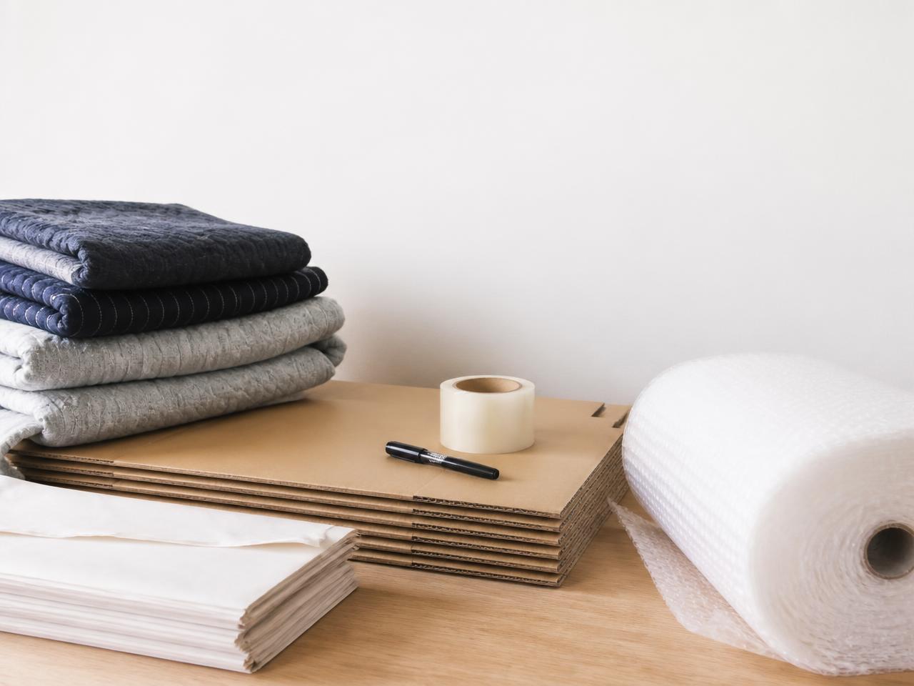 Packmaterial för flytt: flyttkartonger, tejp, bubbelplast, packpapper och filtar på ett bord